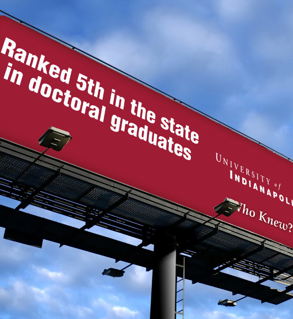 University of Indianapolis billboard advertising ranking 5th in state for doctoral graduates against a blue sky.