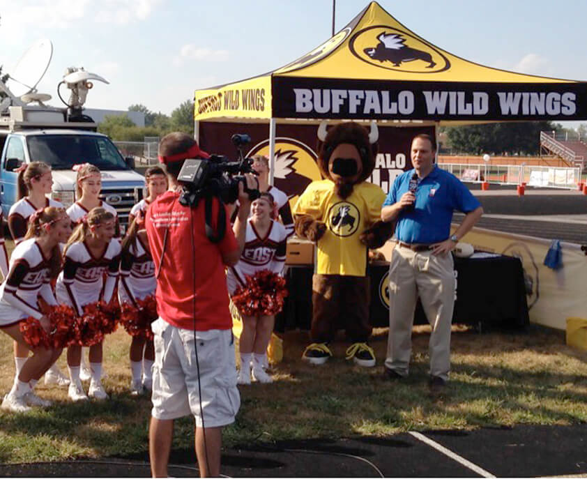 Local sports event with Buffalo Wild Wings booth, mascot, cheerleaders, and a news crew.